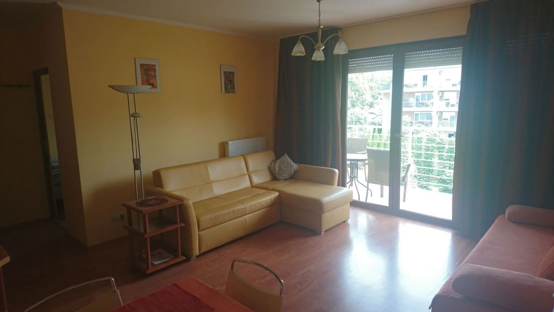 Az apartman nappalija bőr sarokkanapéval, a nagy erkélyajtón át beárad a fény